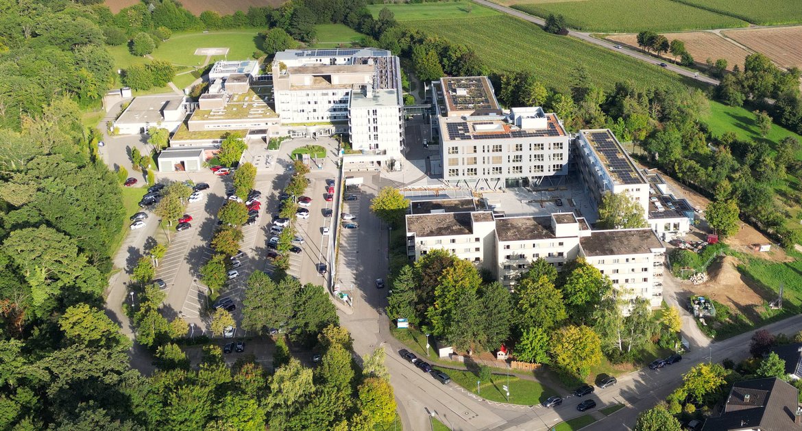 Krankenhaus Mühlacker Enzkreis-Kliniken, RKH, Regionale Kliniken Holding, Campus mit links Krankenhaus, rechts vorne Wohnungen, rechts dahinter Ärztehaus, Kindergarten Rabennest und KÜP Kurzzeitpflege Übergangspflege, links Parkplatz,  rechts Bundesstraße B10 Richtung Illingen, hinten Firma Thyssen-Krupp (grün), dann Gewerbegebiet Waldäcker und Biogasanlage, am Horizont hinten Illingen, Drohnenbild, Luftbild mit Drohne