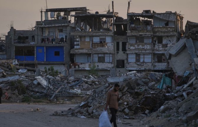 Palästinenser gehen im südlichen Gazastreifen eine Straße entlang, die von Gebäuden umgeben ist, die bei israelischen Luft- und Bodenoperationen zerstört wurden. (Archivbild).<span class='image-autor'>Abdel Kareem Hana/AP/dpa</span>