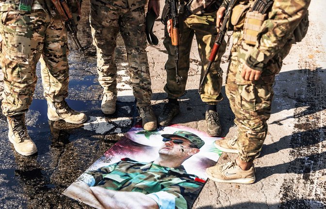 Syrische Kämpfer stehen nach ihrem Sieg auf einem Bild von Assad.<span class='image-autor'>Foto: dpa/Anas Alkharboutli</span>
