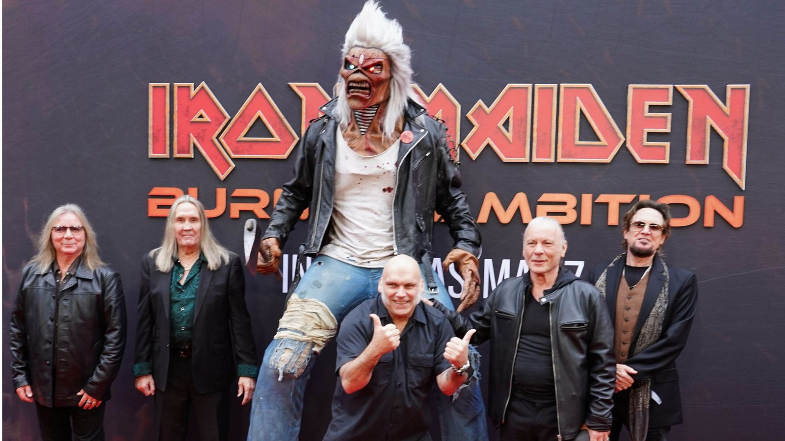 Die Bandmitglieder von Iron Maiden bei der Weltpremiere des Dokumentarfilms „Burining Ambition“ – Maskottchen Eddie darf natürlich nicht fehlen.Foto: Ian West/PA Wire/dpa/Ian West