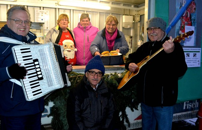 Mit musikalischen Weihnachtsgrüßen verabschiedeten sich die Mitglieder des Angelsportvereins (ASV) Illingen von ihren Gästen am Fischwagen auf dem Schillerplatz in die Winterpause. Am letzten Verkaufstag in diesem Jahr fehlte auch dieses Mal das Trio „Top 3“ nicht. Ottmar Kurbel, Heinz Sibert und Reimund Scheytt erfüllten den Platz mit Melodien bekannter Weihnachtslieder. „Herzlichen Dank an meine Fischwagenband“, freute sich die ASV-Vorsitzende Hedwig Ramstein, die kurzerhand den drei Musikern einen Namen passend zum Auftritt gab. Der ASV bietet schon traditionell über die Wintermonate auf dem Wochenmarkt Räucherfisch sowie Lachs- und Heringsbrötchen zum Verkauf an. Der Erlös fließe in die Vereinskasse, erklärte Ramstein. Unser Bild zeigt die „Fischwagenband“ mit Reimund Scheytt (v.l.), Ottmar Kurbel und Heinz Sibert und dem Fischwagenteam mit Sonja Mahler (v.l), Sabine Fechner und Hedwig Ramstein.  <span class='image-autor'>Foto: Stahlfeld</span>