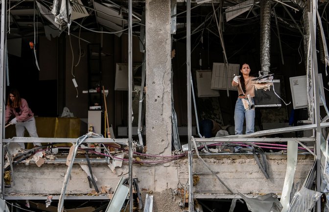 Eine Frau wirft Schutt nach draußen, während sie einen  Friseursalon in Kiew aufräumt, der bei einem russischen Angriff beschädigt wurde.<span class='image-autor'>Foto: Julia Demaree Nikhinson/AP/dpa</span>