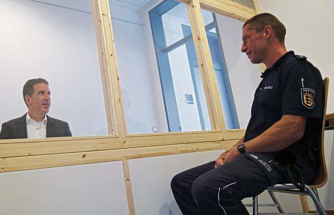JVA-Leiter Frank Jansen (links) und Mitarbeiter Marco Schraft simulieren eine Gesprächssituation, wie sie bei Besuchen von Gefangenen aktuell in den mit Trennscheiben versehenen Räumen möglich ist.  Foto: Friedrich