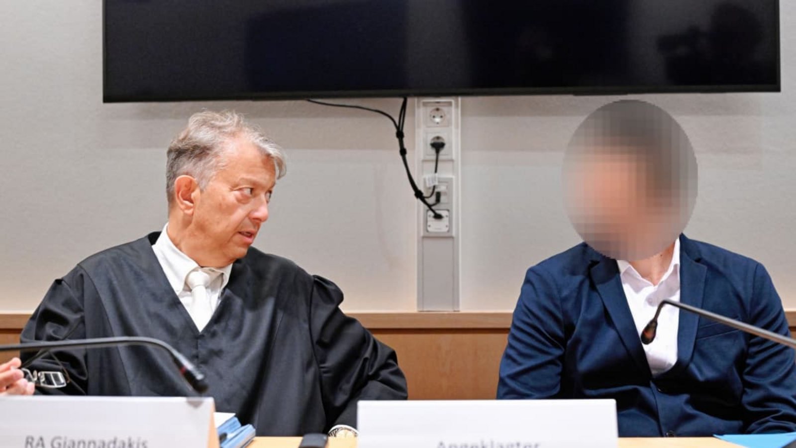 Der Angeklagte (rechts) spricht im Verhandlungssaal des Landgerichts mit seinem Rechtsanwalt Dimitrios Giannadakis. Der 26-Jährige ist wegen Körperverletzung mit Todesfolge angeklagt. Er soll am 2. Februar in der Pfalz von einem Zugbegleiter aufgefordert worden sein, sein Ticket zu zeigen. Im weiteren Verlauf soll der fahrkartenlose Grieche dem 36-Jährigen Faustschläge gegen Kopf und Schläfen versetzt haben. Der Zugbegleiter starb am 4. Februar an einer Hirnblutung.Uwe Anspach/dpa POOL/dpa Der Angeklagte (rechts) spricht im Verhandlungssaal des Landgerichts mit seinem Rechtsanwalt Dimitrios Giannadakis. Der 26-Jährige ist wegen Körperverletzung mit Todesfolge angeklagt. Er soll am 2. Februar in der Pfalz von einem Zugbegleiter aufgefordert worden sein, sein Ticket zu zeigen. Im weiteren Verlauf soll der fahrkartenlose Grieche dem 36-Jährigen Faustschläge gegen Kopf und Schläfen versetzt haben. Der Zugbegleiter starb am 4. Februar an einer Hirnblutung.Uwe Anspach/dpa POOL/dpa
