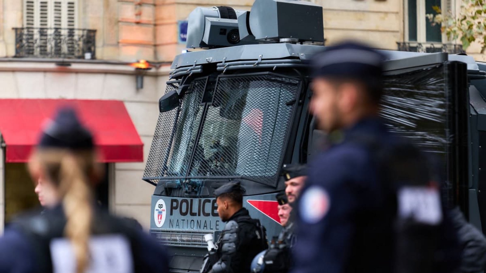 Polizisten in Schutzausrüstung stehen vor einem Wasserwerfer der französischen "Police Nationale" mit vergitterter Frontscheibe.Marcus Golejewski/dpa
