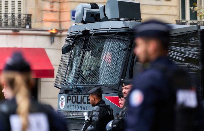 Polizisten in Schutzausrüstung stehen vor einem Wasserwerfer der französischen "Police Nationale" mit vergitterter Frontscheibe.<span class='image-autor'>Marcus Golejewski/dpa</span>