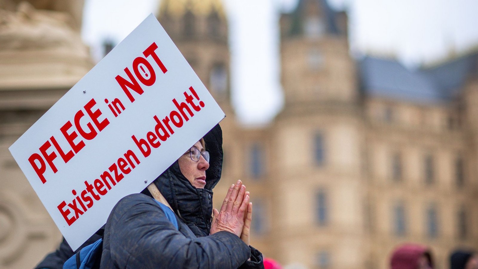 Bei einer Protestaktion vor dem Schweriner Landtag hält eine Teilnehmerin ein Schild mit der Aufschrift "Pflege in Not - Existenzen bedroht!".Foto: Jens Büttner/dpa