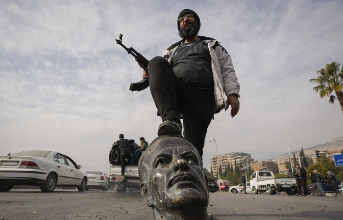 Ein Oppositionskämpfer tritt auf den abgetrennten Kopf einer Statue des verstorbenen syrischen Präsidenten Hafis al-Assad. Die neuen Machthaber in Syrien haben sich mit „allen bewaffneten Gruppen“ auf deren Auflösung geeinigt (Archivfoto).<span class='image-autor'>Foto: dpa/Hussein Malla</span>