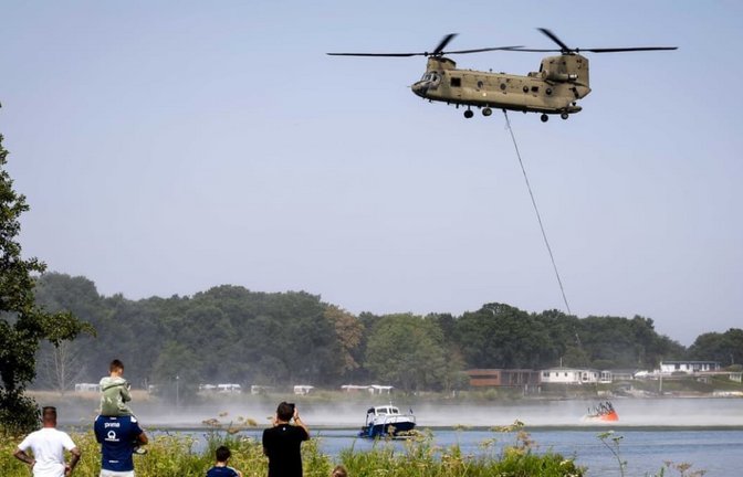 Tagesausflügler beobachten, wie ein Wassersack unter einem Chinook-Hubschrauber in der Maas befüllt wird. Mehrere Löschhubschrauber der Luftwaffe sind im Einsatz, um einen Waldbrand im Naturschutzgebiet Boschhuizerbergen zu bekämpfen. Rund 100 Hektar sind von dem Feuer betroffen.<span class='image-autor'>Sem Van Der Wal/ANP/dpa</span>