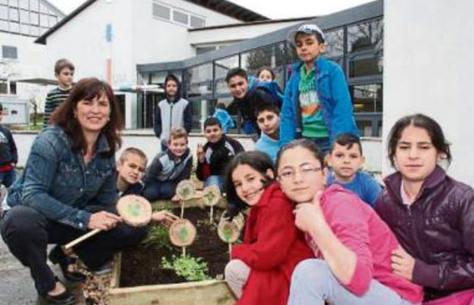 Papp steckt mit den Kindern der Vorbereitungsklasse Holzschilder in den Kräutergarten.