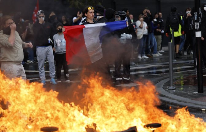 Ein Demonstrant der Protestbewegung «Bloquons Tout» (Alles blockieren) zeigt eine französische Nationalflagge neben brennenden Müllkübeln.<span class='image-autor'>Foto: AP/dpa/Jean-Francois Badias</span>