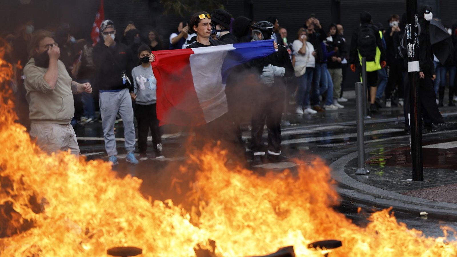Ein Demonstrant der Protestbewegung «Bloquons Tout» (Alles blockieren) zeigt eine französische Nationalflagge neben brennenden Müllkübeln.Foto: AP/dpa/Jean-Francois Badias Ein Demonstrant der Protestbewegung «Bloquons Tout» (Alles blockieren) zeigt eine französische Nationalflagge neben brennenden Müllkübeln.Foto: AP/dpa/Jean-Francois Badias