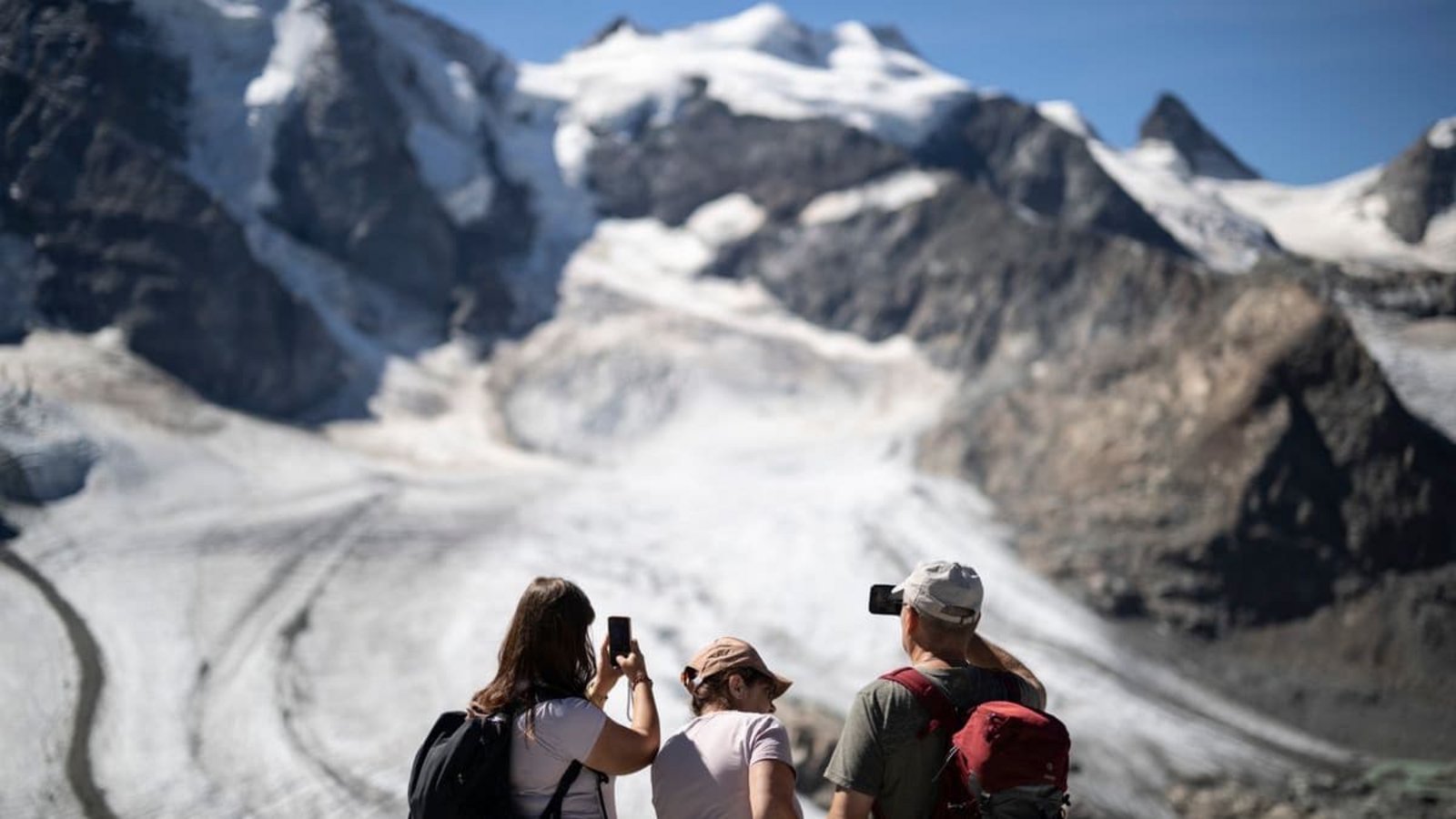 Gletscher in der Schweiz: Was auf den ersten Blick pittoresk wirkt - ein idyllischer Sommertag in den Alpen mit Touristen, die einen Gletscher fotografieren - ist in Wirklichkeit ein Warnsignal. Die Alpengletscher schmelzen immer schneller dahin.Gian Ehrenzeller/Keystone/dpa Gletscher in der Schweiz: Was auf den ersten Blick pittoresk wirkt - ein idyllischer Sommertag in den Alpen mit Touristen, die einen Gletscher fotografieren - ist in Wirklichkeit ein Warnsignal. Die Alpengletscher schmelzen immer schneller dahin.Gian Ehrenzeller/Keystone/dpa
