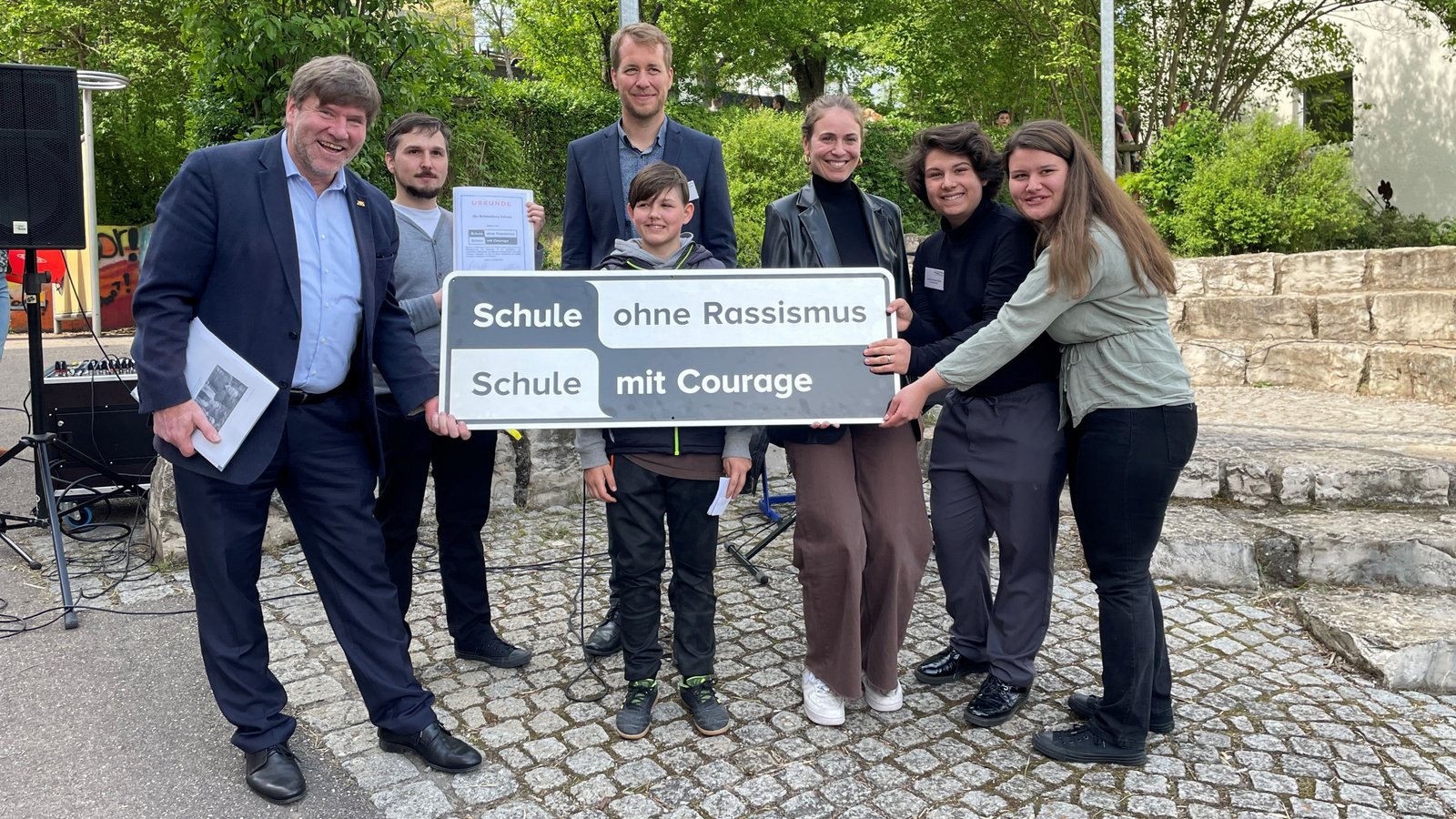 Markus Rösler (links), Andreas Haiß, Jürgen Joos (hinten) und Sophia Oster (Dritte von rechts) zeigen die Plakette, welche ihre Aufnahme im Antirassismus-Schulnetzwerk bestätigt. Foto: Stogios