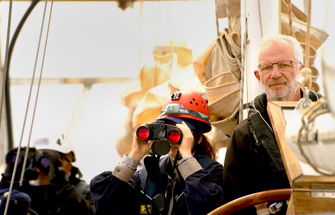 Friedhold Ulonska am Steuer eines Segelschiffs auf dem Mittelmeer – während eine Kollegin aus der Crew mit dem Fernglas nach Flüchtlingen in Seenot Ausschau hält.<span class='image-autor'>Foto: Resqship/
Leon Salner</span>