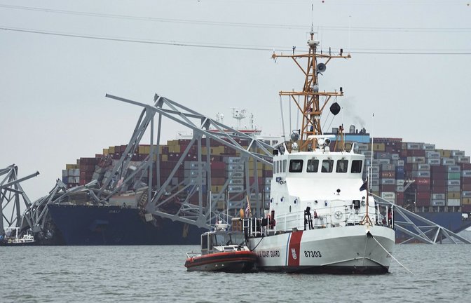 Ein Kutter der Küstenwache patrouilliert vor einem Containerschiff, das unter einem Teil der Francis Scott Key Bridge festsitzt.<span class='image-autor'>Foto: dpa/Steve Helber</span>