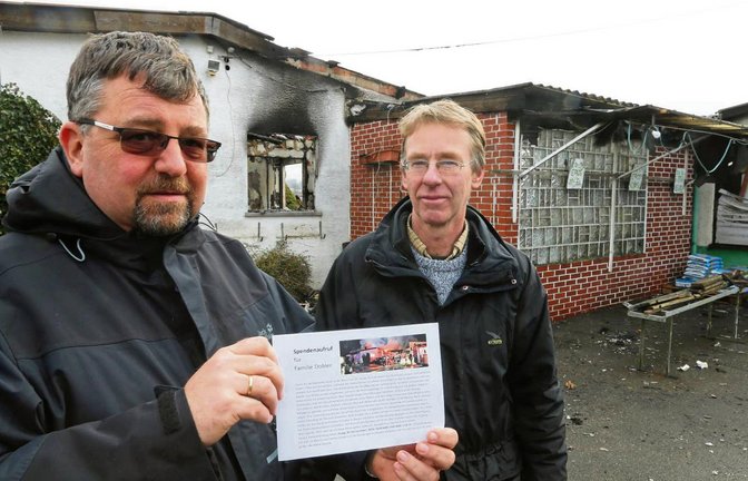 Sersheims Pfarrer Johannes Rau und Thomas Dobler mit dem Spendenaufruf der Kirchengemeinde vor der Brandruine an der Gärtnerei. Fotos: Küppers
