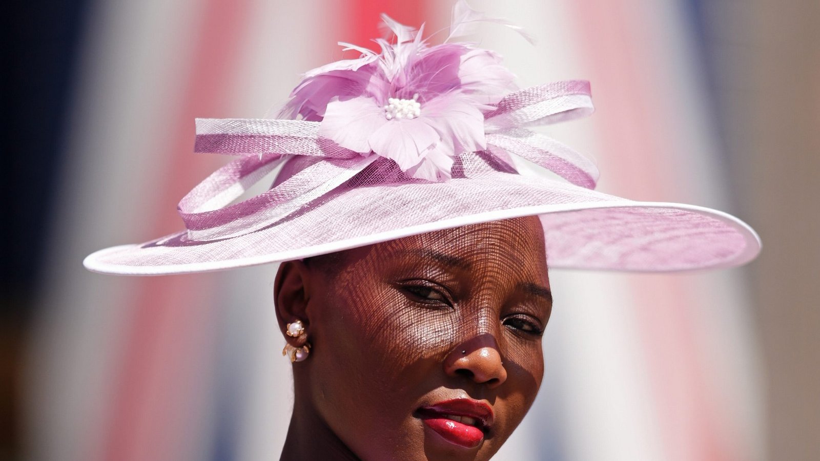 Eine Besucherin von Royal Ascot trägt einen zartrosa Tellerhut mit breiter Krempe, Schleifenband und Blütendetail. Der transparente Stoff wirft feine Schatten auf das Gesicht und verleiht dem Ton-in-Ton-Look eine elegante, sommerliche Wirkung.Foto: picture alliance/dpa/PA Wire | John Walton