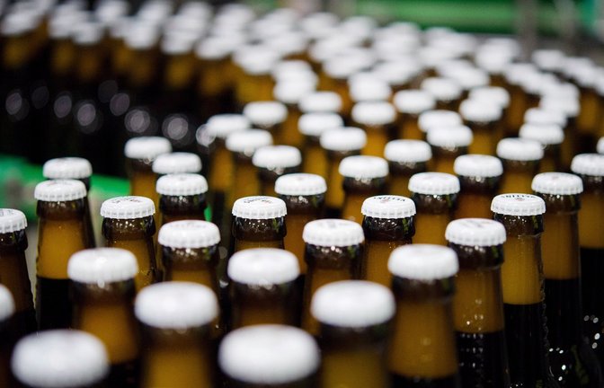 Bierflaschen mit Kronkorken laufen durch die Produktion einer Brauerei über die Förderbänder einer Befüllungsanlage.<span class='image-autor'>Foto: Rainer Jensen/dpa</span>