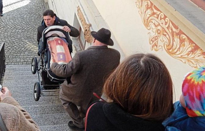 Wie kommt man mit einem Kinderwagen in die Sitzungsräume des Vaihinger Rathauses? Eigentlich gar nicht. Es sei denn, man hat tatkräftige Hilfe. Die bekam in dieser Woche die Stadträtin Susanne Schwarz-Zeeb (Bündnis 90/Die Grünen), als sie mit Enkelin Anna zur gemeinsamen Pressekonferenz der Vaihinger Stadtratsfraktionen mit dem Thema Bürgerentscheid wollte. Eberhard Zucker (Freie Wähler) und Eberhard Berg (SPD) packten mit an und transportieren den Kinderwagen über die Treppen. Die kleine Anna (ein Jahr alt) ertrug dann auch die Ausführungen zum Enßle-Areal klaglos. Ihr genügte eine Brezel, an der sie nach dem Schläfchen vergnügt kaute. Foto: Arning
