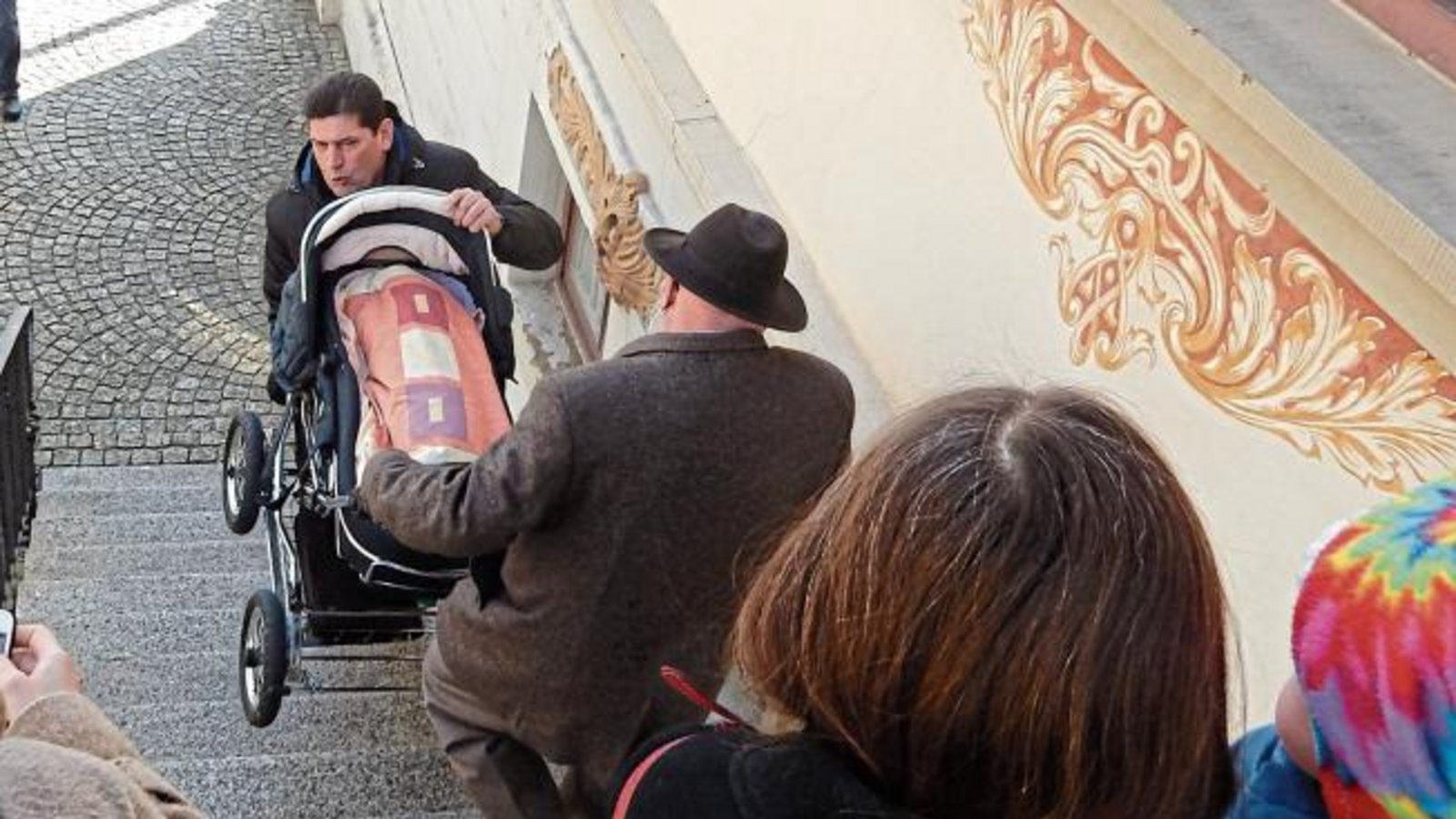 Wie kommt man mit einem Kinderwagen in die Sitzungsräume des Vaihinger Rathauses? Eigentlich gar nicht. Es sei denn, man hat tatkräftige Hilfe. Die bekam in dieser Woche die Stadträtin Susanne Schwarz-Zeeb (Bündnis 90/Die Grünen), als sie mit Enkelin Anna zur gemeinsamen Pressekonferenz der Vaihinger Stadtratsfraktionen mit dem Thema Bürgerentscheid wollte. Eberhard Zucker (Freie Wähler) und Eberhard Berg (SPD) packten mit an und transportieren den Kinderwagen über die Treppen. Die kleine Anna (ein Jahr alt) ertrug dann auch die Ausführungen zum Enßle-Areal klaglos. Ihr genügte eine Brezel, an der sie nach dem Schläfchen vergnügt kaute. Foto: Arning