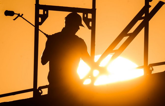 Ein Bauarbeiter steht mit einem Gasbrenner beim Bau eines Mehrfamilienhauses, als am Horizont die Sonne aufgeht.<span class='image-autor'>Foto: dpa/Julian Stratenschulte</span>