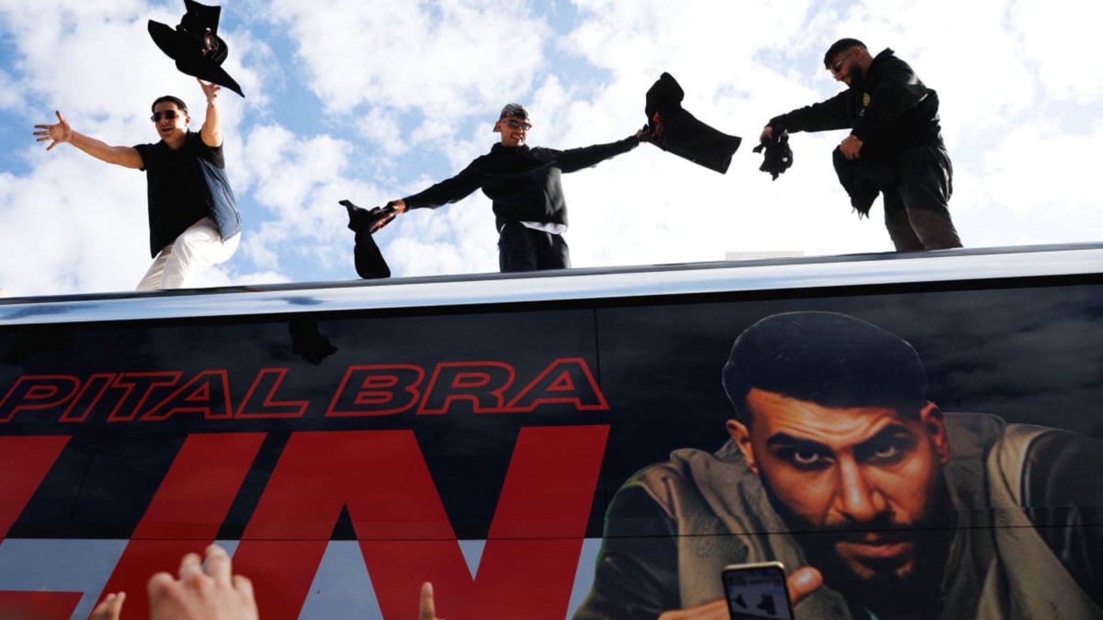 Die Rapper Lacazette, Capital Bra und Samra werfen bei einer Fanaktion in Kreuzberg T-Shirts von einem Tourbus.Carsten Koall/dpa Die Rapper Lacazette, Capital Bra und Samra werfen bei einer Fanaktion in Kreuzberg T-Shirts von einem Tourbus.Carsten Koall/dpa