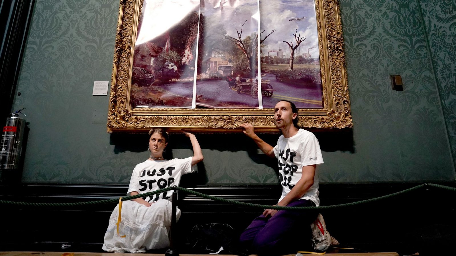 Klimaaktivisten der Organisation Just Stop Oil haben ihre Hände an den Rahmen des Gemäldes "The Hay Wain" von John Constable geklebt, das sie zunächst mit einer auf Poster gedruckten dystopischen Version des Bildes verkleidet hatten.Foto: Kirsty O'connor/PA Wire/dpa