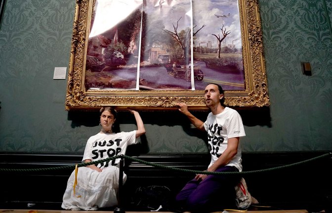 Klimaaktivisten der Organisation Just Stop Oil haben ihre Hände an den Rahmen des Gemäldes "The Hay Wain" von John Constable geklebt, das sie zunächst mit einer auf Poster gedruckten dystopischen Version des Bildes verkleidet hatten.<span class='image-autor'>Foto: Kirsty O'connor/PA Wire/dpa</span>