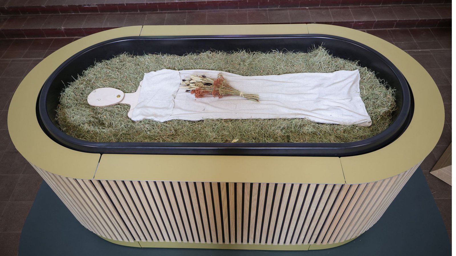 Heu, Stroh, Blumen und eine Holzfigur liegen in einem sogenannten „Kokon“ bei einem Pressegespräch zu der neuen Bestattungsform „Reerdigung“ in der Kapelle auf dem Kieler Parkfriedhof Eichhof.Foto: dpa/Christian Charisius Heu, Stroh, Blumen und eine Holzfigur liegen in einem sogenannten „Kokon“ bei einem Pressegespräch zu der neuen Bestattungsform „Reerdigung“ in der Kapelle auf dem Kieler Parkfriedhof Eichhof.Foto: dpa/Christian Charisius