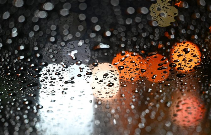 Stuttgart: Lichter von Fahrzeugen scheinen durch eine Autoscheibe, die mit Regentropfen bedeckt ist.<span class='image-autor'>Foto: Bernd Weißbrod/dpa/Bernd Weißbrod</span>