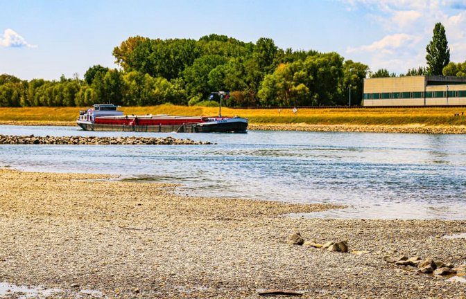 Durch das extreme Niedrigwasser liegen im Bereich des Pegels Maxau Steine im Flussbett des Rheins trocken, während im Hintergrund ein Binnenschiff vorbeifährt.<span class='image-autor'>Thomas Riedel/dpa</span>
