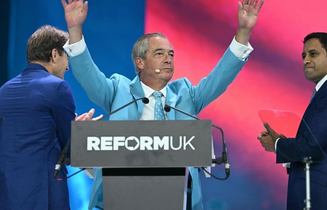 Der Chef der Reform UK Partei, Nigel Farage, wird nach seiner Rede auf dem Parteitag in Birmingham gefeiert. Auf der Bühne spenden ihm der stellvertretende Vorsitzende Richard Tice (L) und der Schatten-Innenminister Zia Yusuf Beifall.<span class='image-autor'>Oli Scarff/afp</span>
