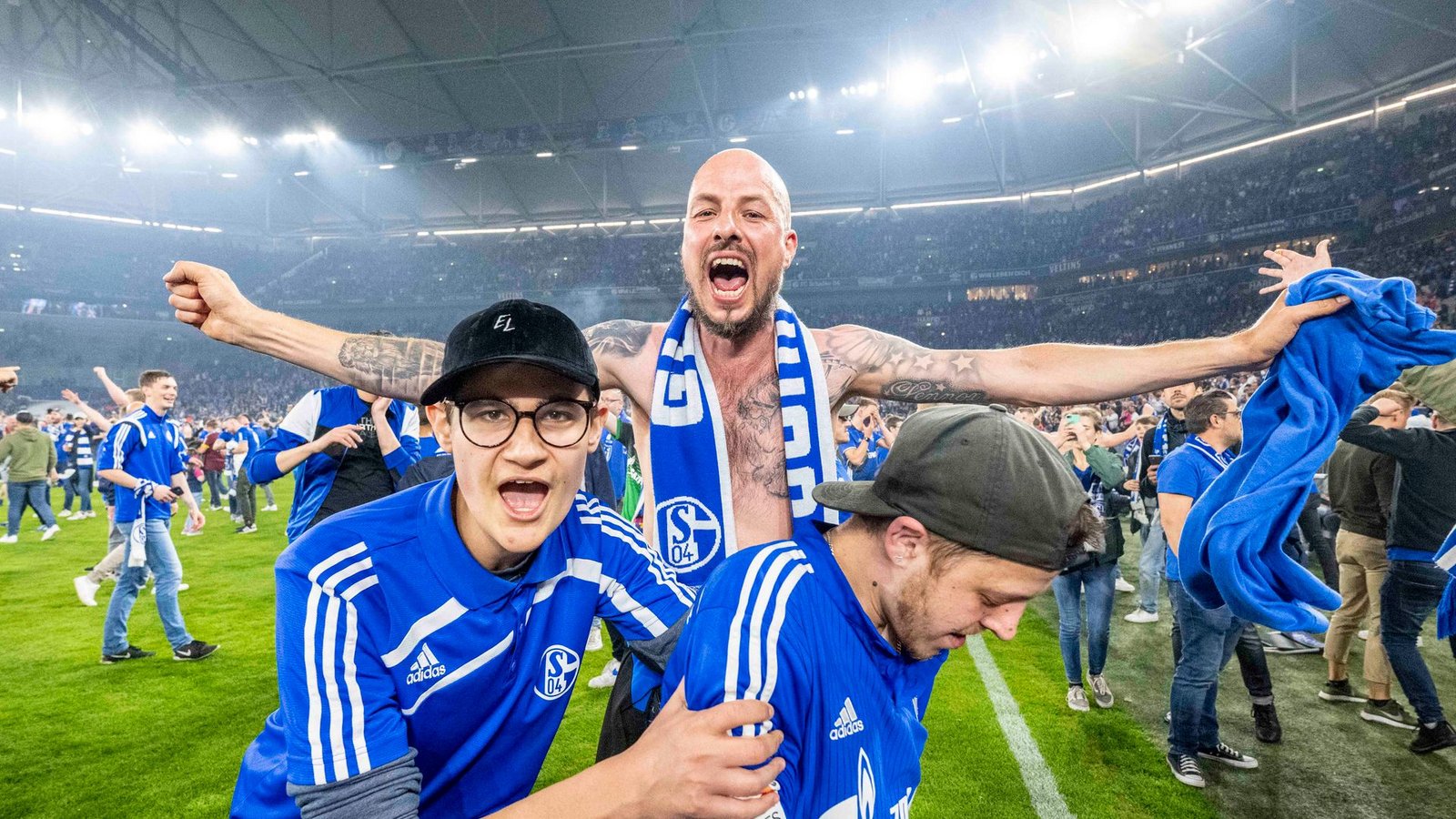 Schalker Fans haben den Rasen gestürmt und bejubeln den Aufstieg.Foto: David Inderlied/dpa