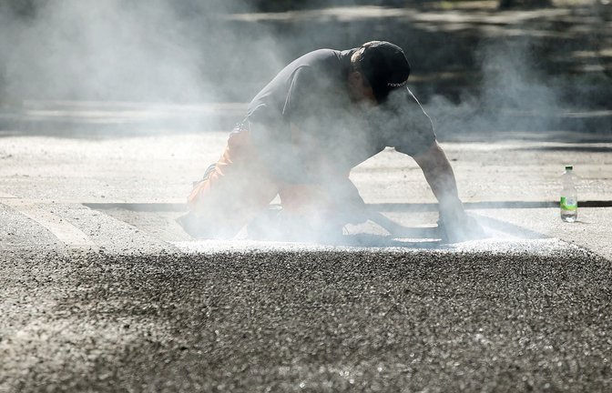 Ein Bauarbeiter repariert eine Straße in Berlin mit Bitumen, einem Bindemittel für Asphalt. (Symbolbild)<span class='image-autor'>Foto: Wolfgang Kumm/dpa</span>