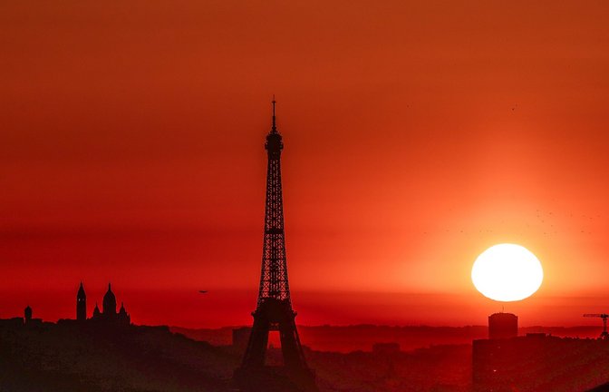 Die Sonne geht Anfang Juli 2025 über dem Eiffelturm und der Basilika Sacre Coeur auf dem Montmartre-Hügel auf, während in der Stadt wegen der hohen Temperaturen Alarmstufe Rot herrscht:<span class='image-autor'>Foto: Thibaud Moritz/AFP/dpa</span>