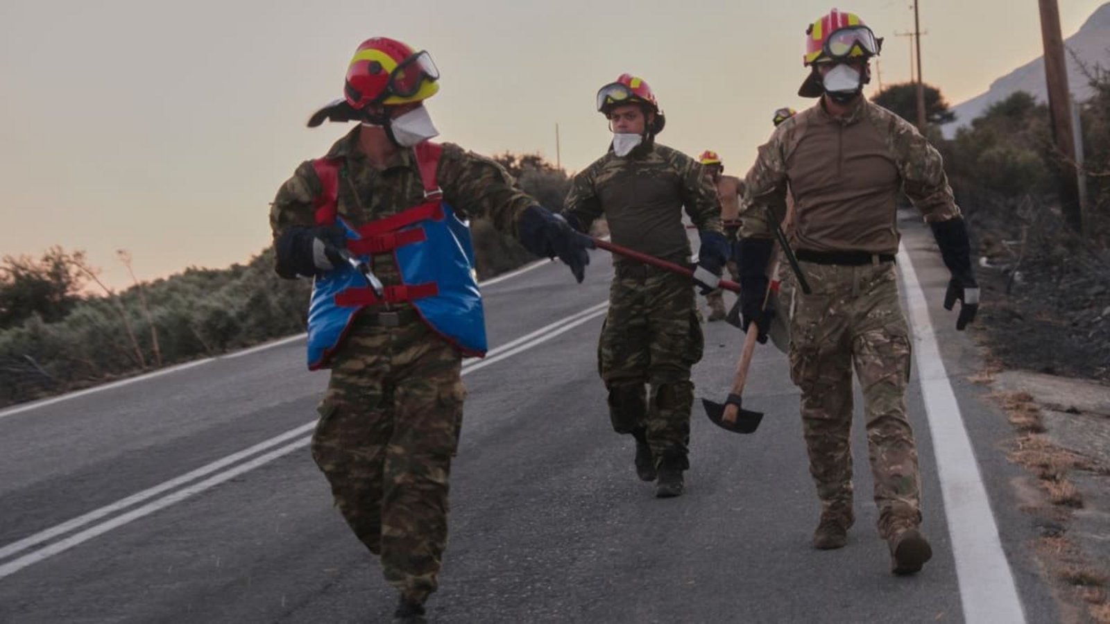 Feuerwehrleute gehen während eines Waldbrands in der Region Rethymno auf der südgriechischen Insel Kreta mit Werkzeugen eine Straße entlang.Giannis Angelakis/AP/dpa Feuerwehrleute gehen während eines Waldbrands in der Region Rethymno auf der südgriechischen Insel Kreta mit Werkzeugen eine Straße entlang.Giannis Angelakis/AP/dpa