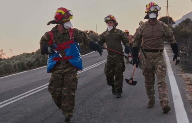 Feuerwehrleute gehen während eines Waldbrands in der Region Rethymno auf der südgriechischen Insel Kreta mit Werkzeugen eine Straße entlang.<span class='image-autor'>Giannis Angelakis/AP/dpa</span>