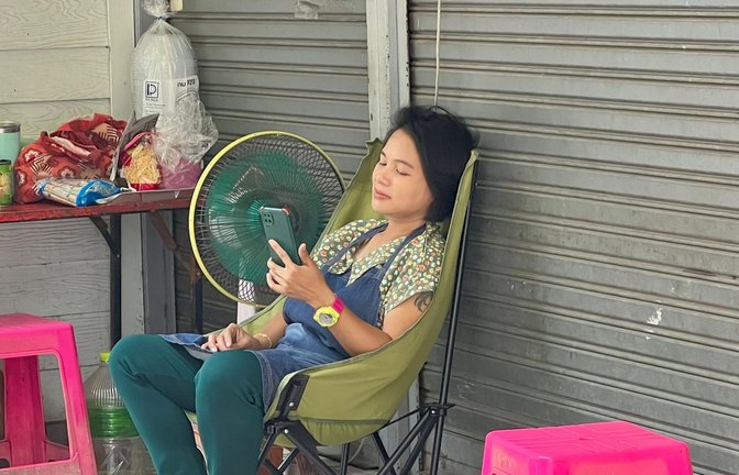 Im Schatten und mit Ventilator: Eine Frau in Bangkok versucht, sich sich abzukühlen.<span class='image-autor'>Foto: Carola Frentzen/dpa</span>