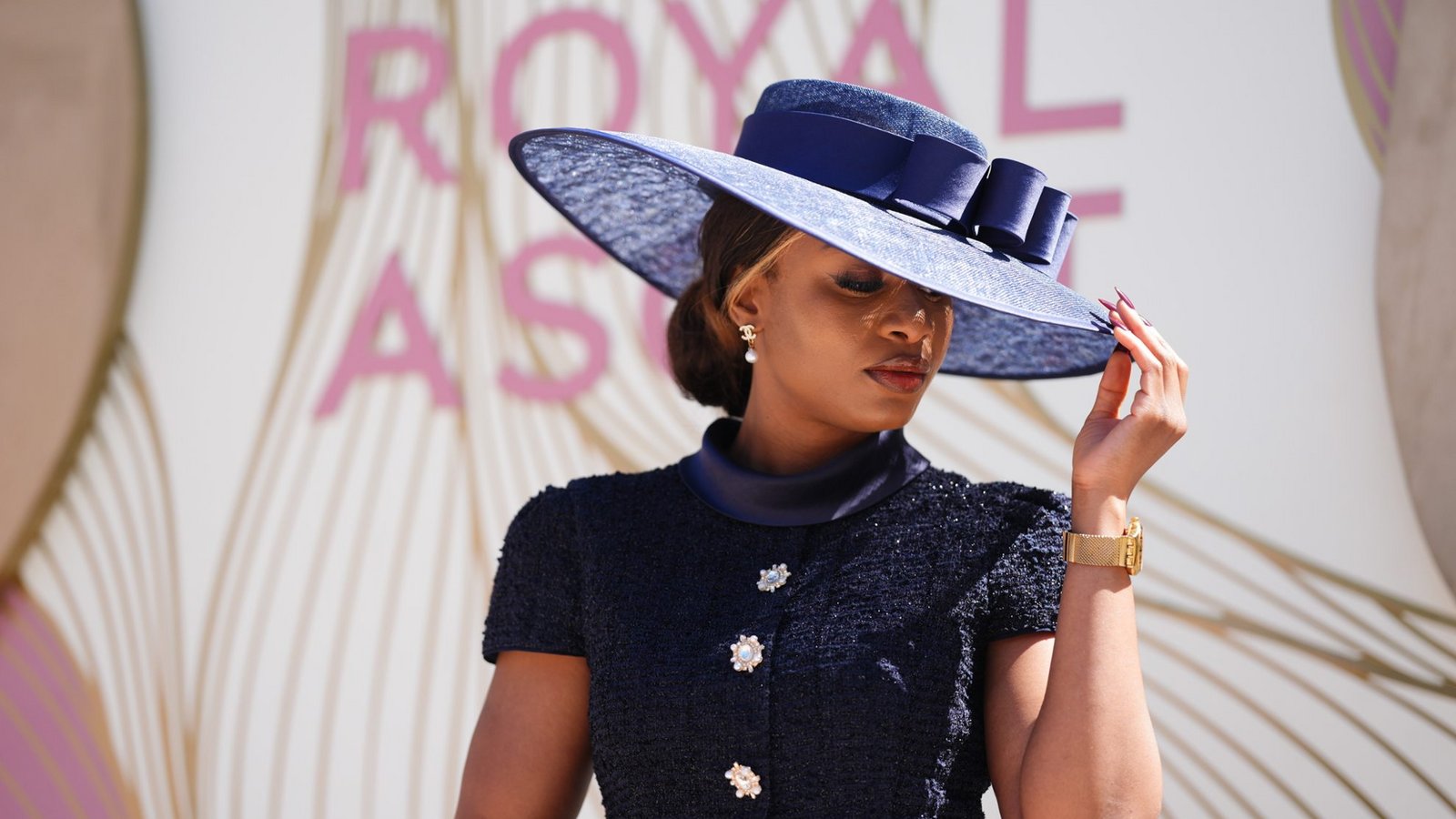 Eine Besucherin von Royal Ascot zeigt einen besonders eleganten Ton-in-Ton-Look in Dunkelblau: Der breitkrempige Hut mit Schleifendetail passt zum strukturierten Kleid mit Schmuckknöpfen und wirkt klassisch, zurückhaltend und sehr edel.Foto: picture alliance/dpa/PA Wire | John Walton