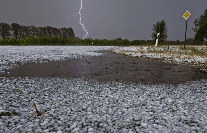Hagelkörner liegen auf einer Fahrbahn bei Wagenfeld in Niedersachsen, während sich ein Blitz im Hintergrund entlädt. Schwere Unwetter sind über Teilen Niedersachsens niedergegangen.<span class='image-autor'>Thomas Lindemann/Nord-West-Media TV /dpa</span>