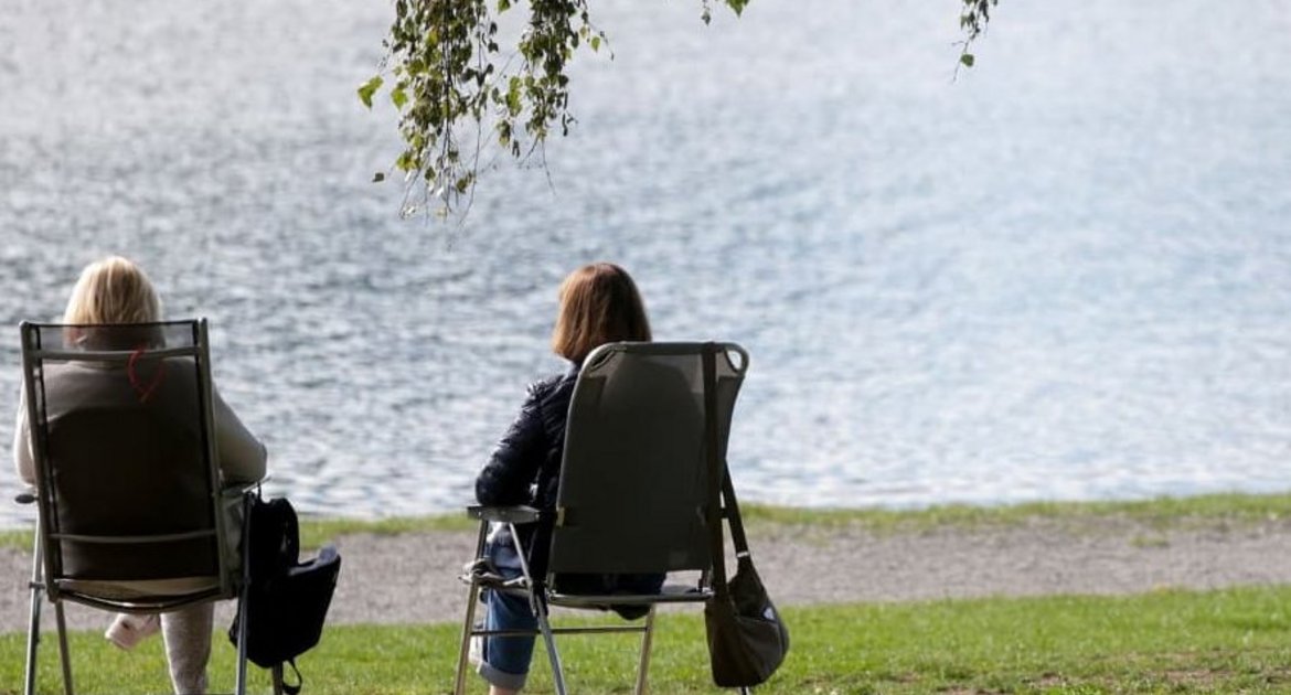 Zwei Frauen sitzen auf Klappstühlen an einem See in der Sonne. (Symbolbild)