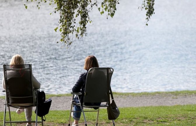 Zwei Frauen sitzen auf Klappstühlen an einem See in der Sonne. (Symbolbild)<span class='image-autor'>Thomas Warnack/dpa</span>