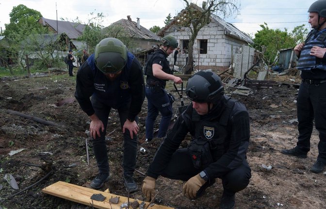 Ein ukrainischer Polizeibeamter und ein Staatsanwalt für Kriegsverbrechen inspizieren Bruchstücke einer Gleitbombe vor einem beschädigten Haus nach einem russischen Luftangriff auf ein Wohnviertel.<span class='image-autor'>Foto: Evgeniy Maloletka/AP/dpa</span>