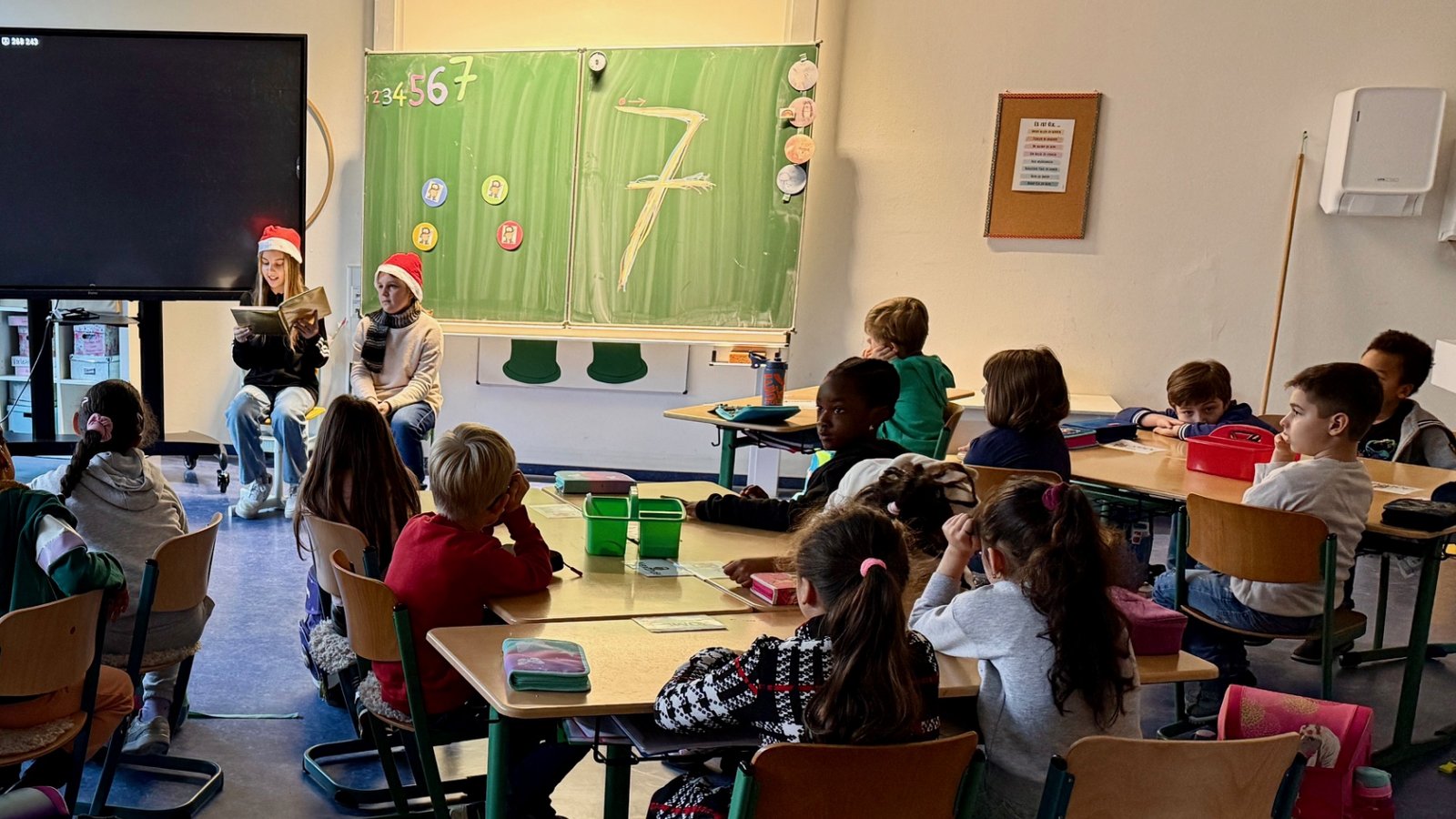 Die Klasse 6b der Ferdinand-Steinbeis-Realschule und ihre Klassenlehrerin Ute Heinrichs möchten in der Vorweihnachtszeit Freude verschenken. Deshalb lesen die Sechstklässler zwei Mal in der Woche in die ersten Klassen der Schlossbergschule vor. Die ersten Klassen sind seit diesem Jahr im Gebäude der FSR untergebracht. Kontakt besteht aber kaum, da die Erstklässler im Anbau sind und einen eigenen Eingang benutzen. Nun wollte die 6b die „Kleinen“ im Schulgebäude einfach mal willkommen heißen und ihnen mit Geschichten eine Freude bereiten. Jetzt war es soweit: Zwei Sechstklässlerinnen zogen mit dem goldenen Geschichtenbuch und zwei Weihnachtsmützen auf dem Kopf in Richtung 1d. Mit großen Augen und voller Konzentration lauschten die Kleinen den zwei Großen, als sie ihre Vorweihnachtsgeschichte – zuvor fleißig geübt – vorlasen. Immer dienstags und freitags werden nun zwei Sechstklässler in die ersten Klassen gehen.  Foto: p