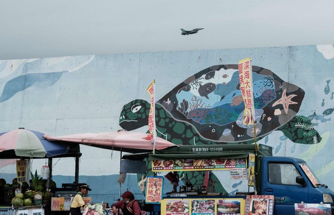 Streetfood und Streitkräfte: Eine Straßenszene in Hualien, einer Stadt im Osten Taiwans. Im Hintergrund hebt ein taiwanesischer F-16-Kampfjet von einer Militärbasis ab.<span class='image-autor'>Foto: AFP/Yasuyoshi Chiba</span>
