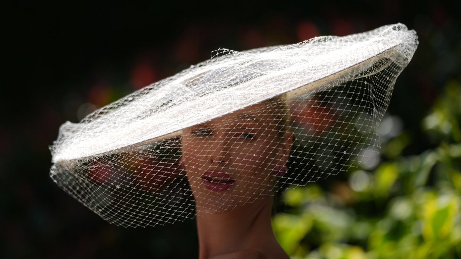 Eine Besucherin von Royal Ascot trägt einen eleganten weißen Tellerhut mit feinem Netzschleier, der das Gesicht teilweise bedeckt. Der reduzierte Look wirkt deutlich klassischer und zurückhaltender als viele der farbenfrohen Statement-Hüte.Foto: picture alliance/dpa/AP | Alastair Grant
