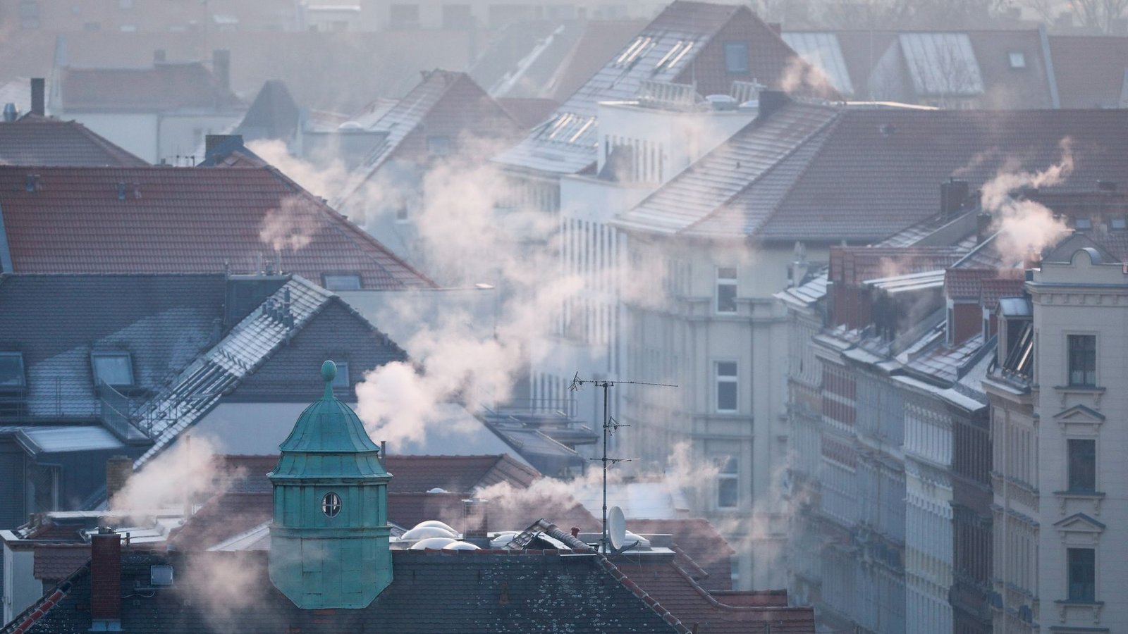 Rauch strömt aus Kaminen auf Dächern von Mehrfamilienhäuser.Foto: Jan Woitas/dpa