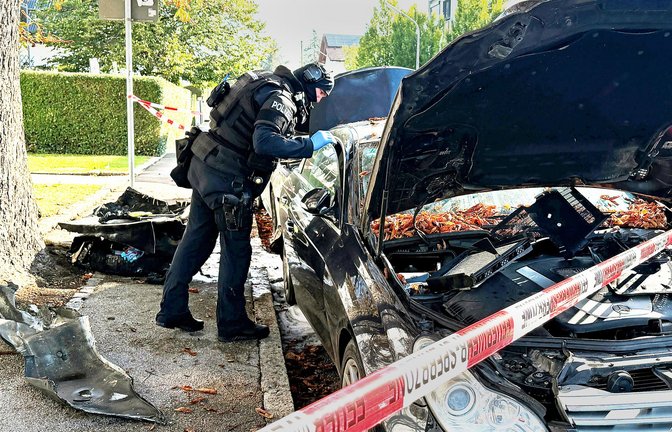 Ein Polizist mit Schutzweste steht an einem PKW, der gebrant hatte. Ein Brand in einem Münchner Einfamilienhaus hat einen Großeinsatz von Polizei und Feuerwehr ausgelöst.<span class='image-autor'>Foto: Roland Freund/dpa/Roland Freund</span>