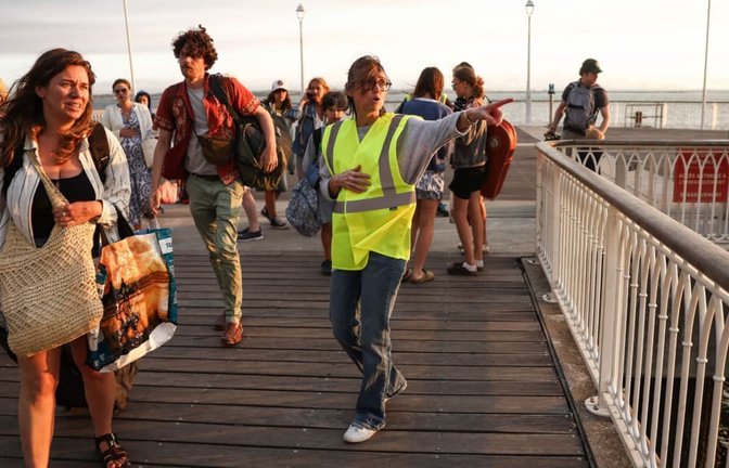 Ein Freiwilliger gibt Urlaubern aus Lege-Cap-Ferret bei ihrer Ankunft per Boot Anweisungen, während sich ein Waldbrand in der Region ausbreitet.<span class='image-autor'>Romain Perrocheau/AFP/dpa</span>